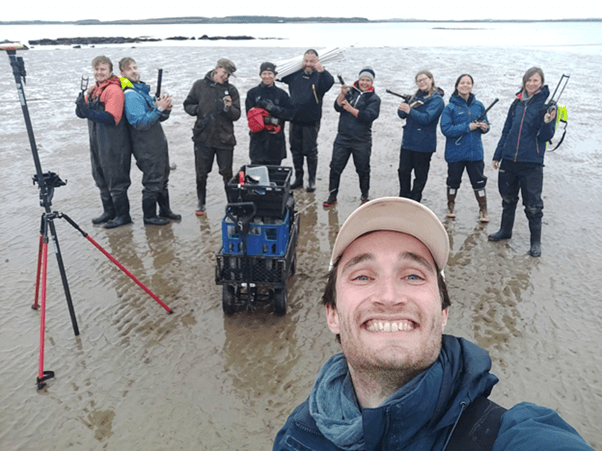 Volunteers supporting seagrass restoration work in Holyhead North Wales. The volunteers are standing in a line holding seagrass restoration equipment.